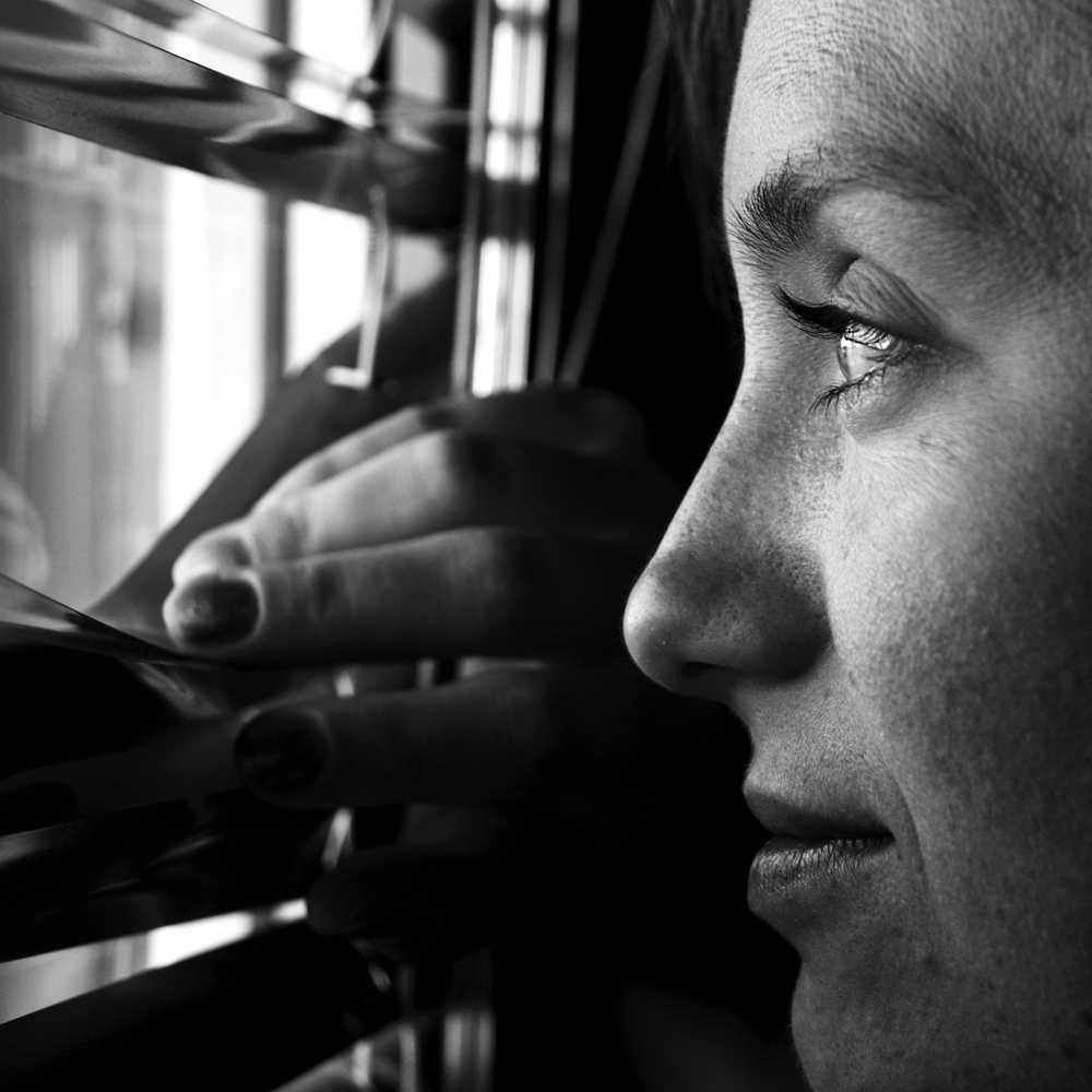 smiling woman looking hopefully into the distance through the window blinds