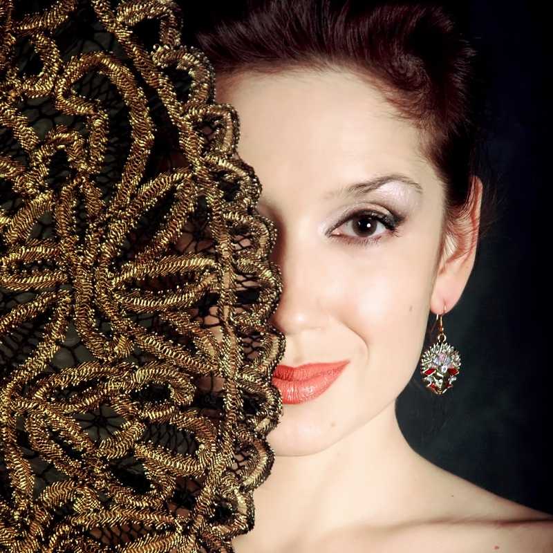 portrait of young lady with a theatre mask earring and a sly smile that hides her face behind a fan