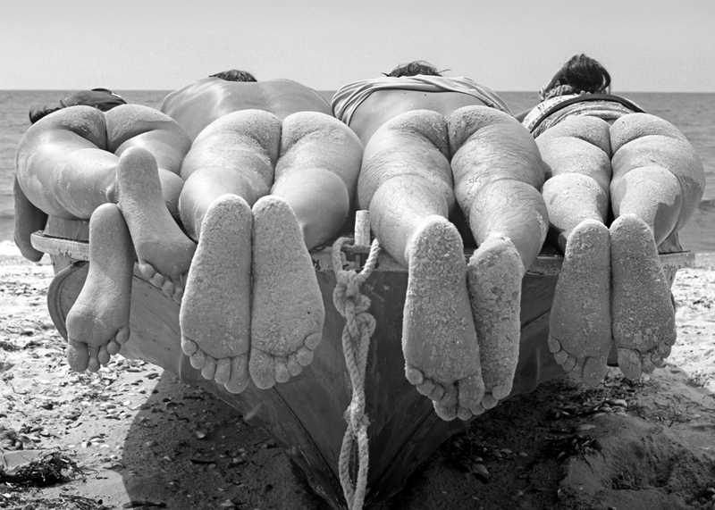 four young people lie naked on old boat near seashore exposing their bottoms and feet to the sun not worrying about anything