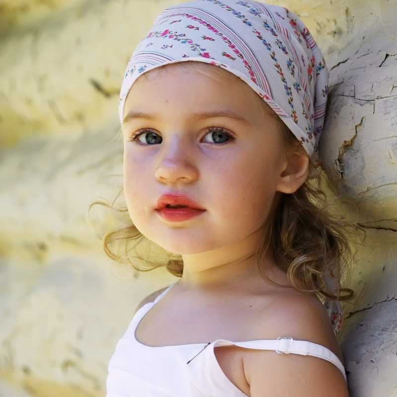 little girl in a headscarf and a blouse with a lowered shoulder strap on the wooden wall background