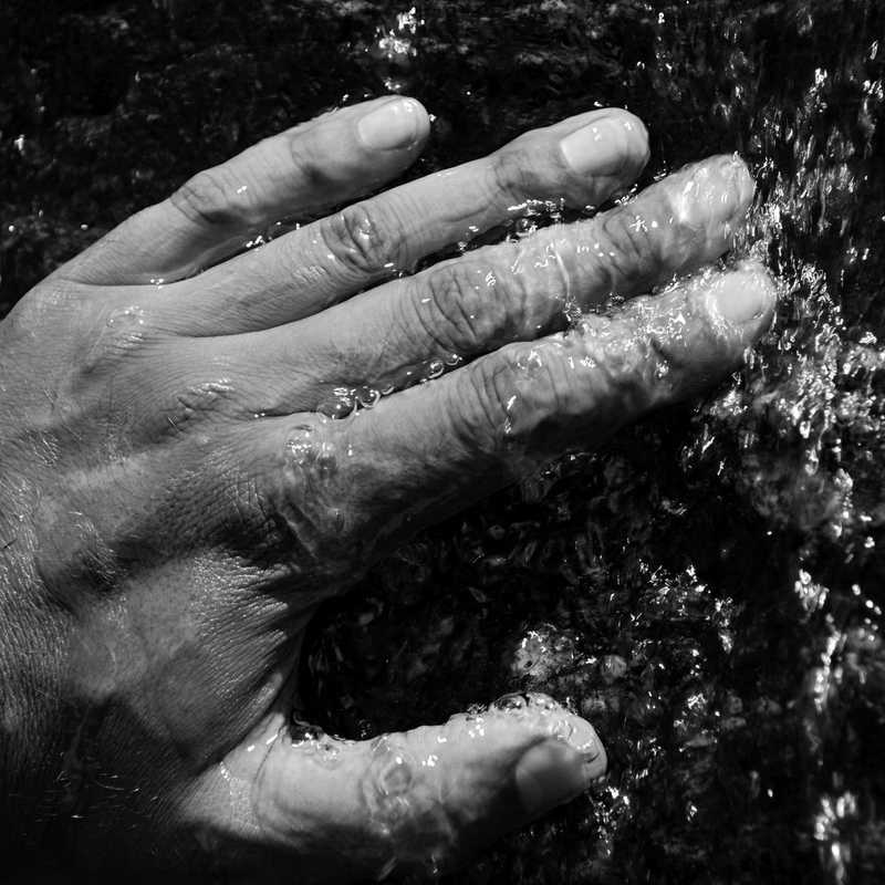 glacial stream water flows through the long fingers of a strong man hand 